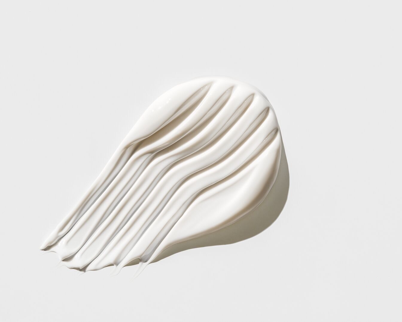 Kremowa, biała maź o gładkiej teksturze, ułożona w równoległe linie na jasnym tle, idealna do pielęgnacji skóry.