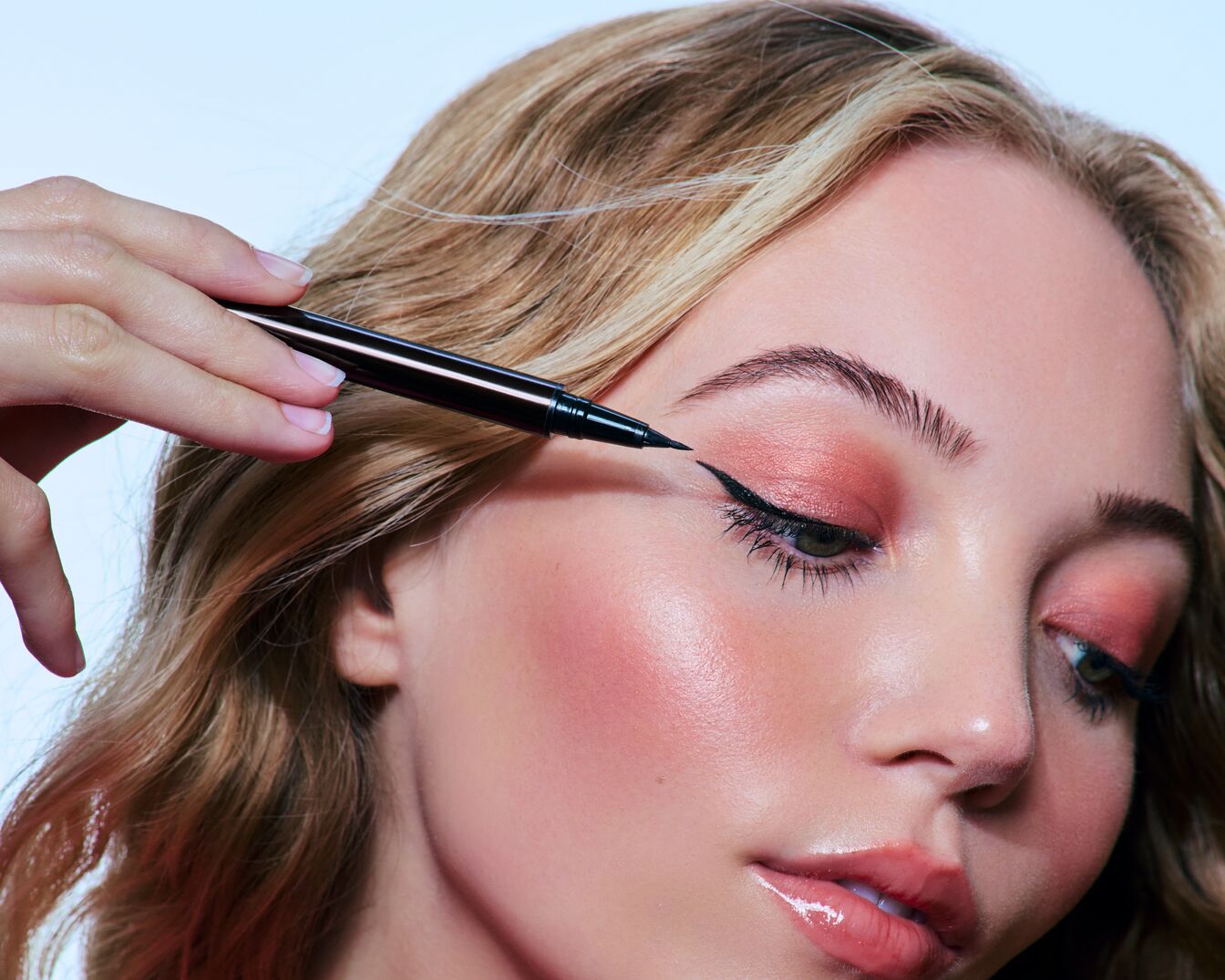 Eine Frau mit blonden Haaren trägt schwarzen Eyeliner mit einem Stift, um einen präzisen und eleganten Look zu erzielen.