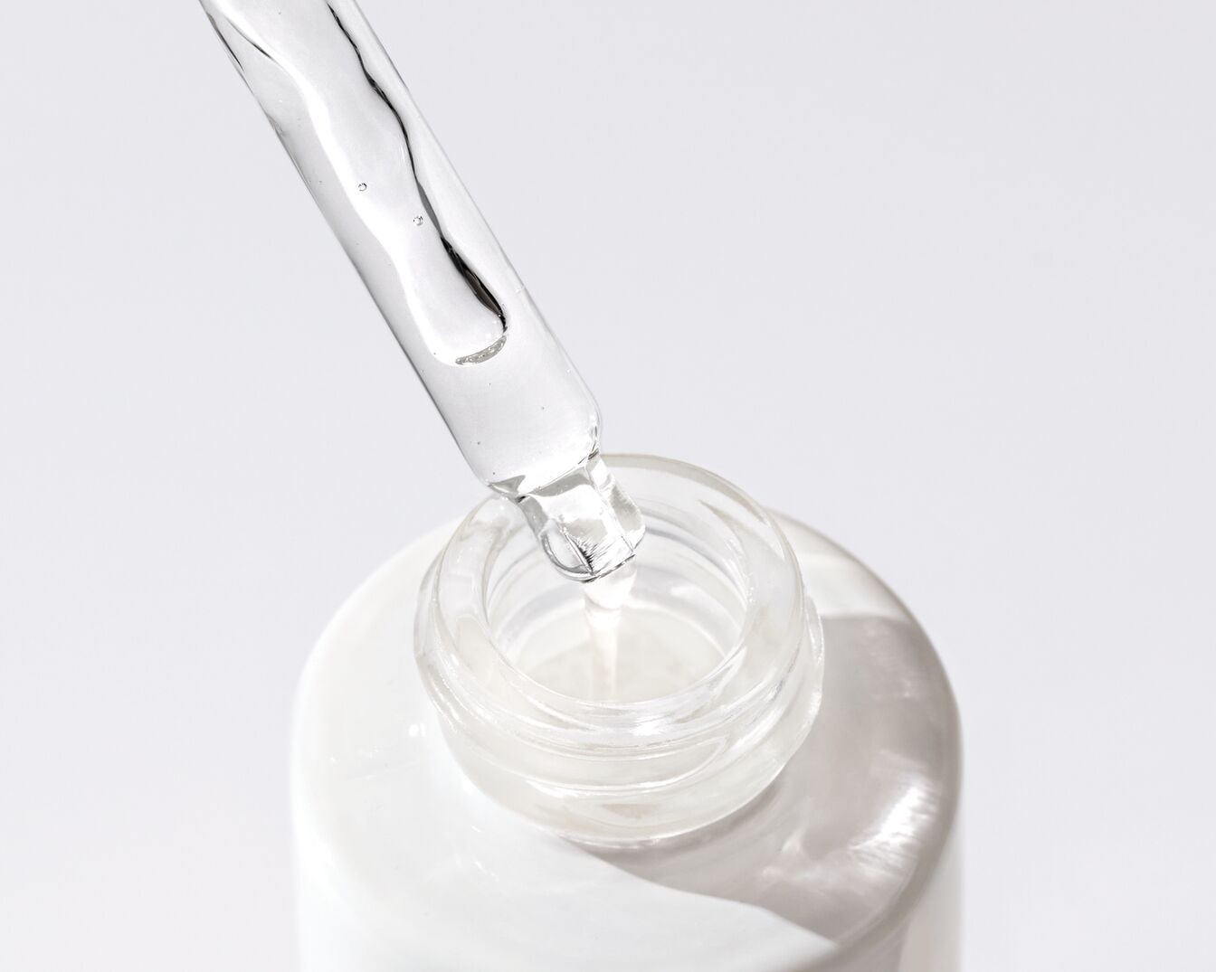 Gotero transparente que extrae suero de una botella blanca, ideal para el cuidado de la piel.