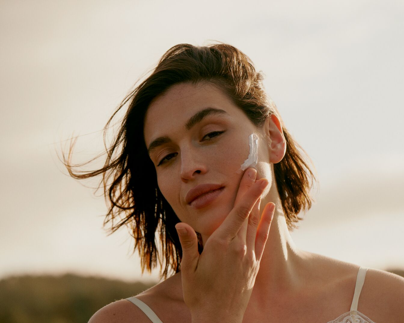 Kobieta delikatnie nakłada biały krem na policzek, promując pielęgnację skóry.