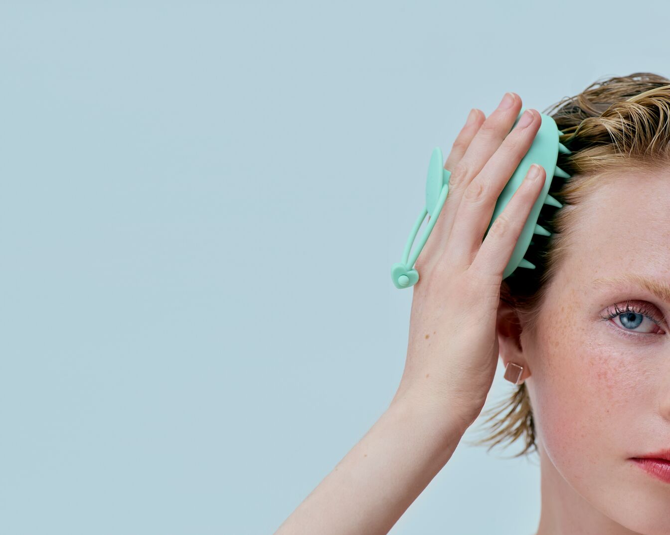 Eine Frau mit blonden, nassen Haaren massiert ihre Kopfhaut mit einer hellgrünen Bürste, um die Durchblutung anzuregen und die Haargesundheit zu fördern.