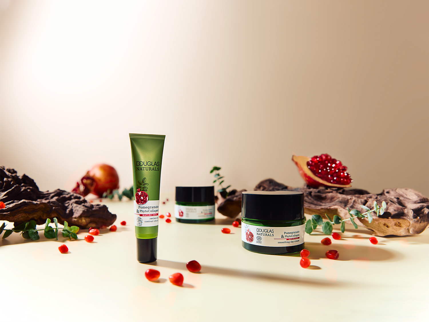 Douglas Naturals Pomegranate & PhytoCollagen huidverzorgingslijn, inclusief reviver contourcrème in een groene tube en gladmakende dagcrème in een zwarte pot, geaccentueerd met granaatappel.