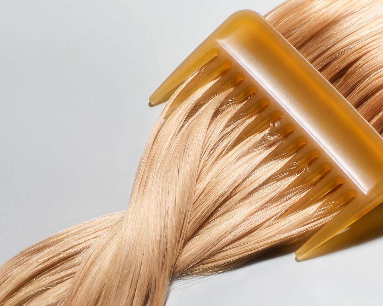 Een close-up van een honingkleurige kam die door glanzend, lichtblond haar glijdt, wat de zachtheid en gladheid van het haar benadrukt.