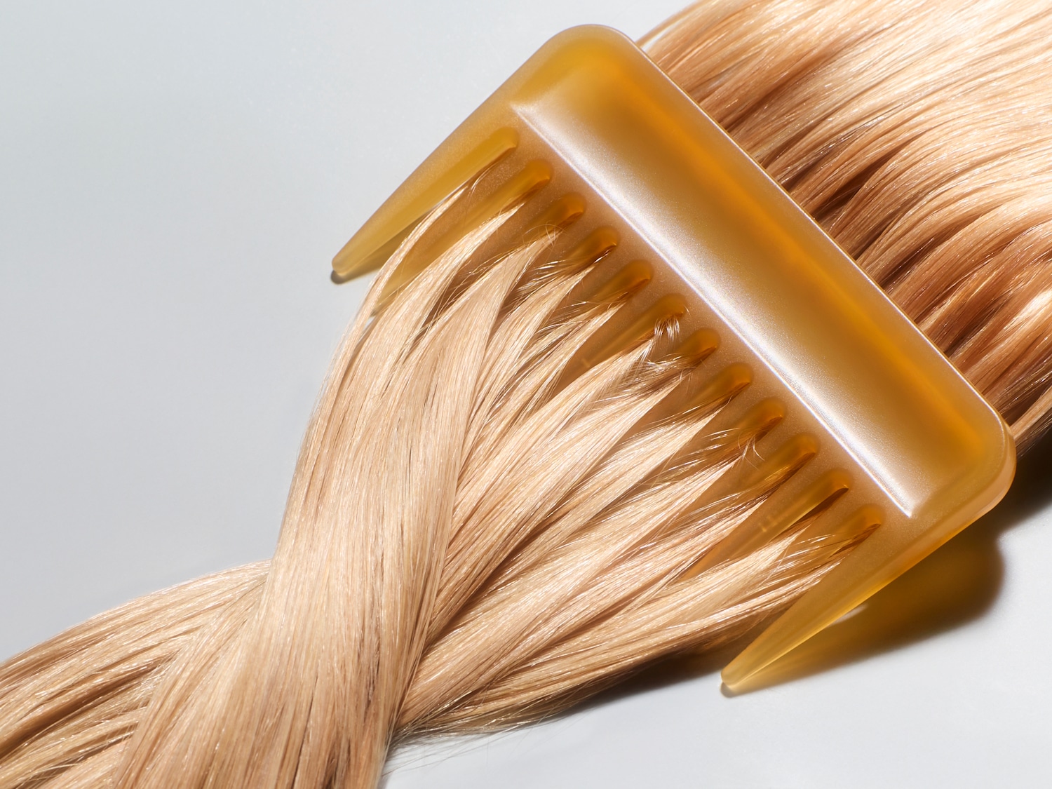 Een close-up van een honingkleurige kam die door glanzend, lichtblond haar glijdt, wat de zachtheid en gladheid van het haar benadrukt.