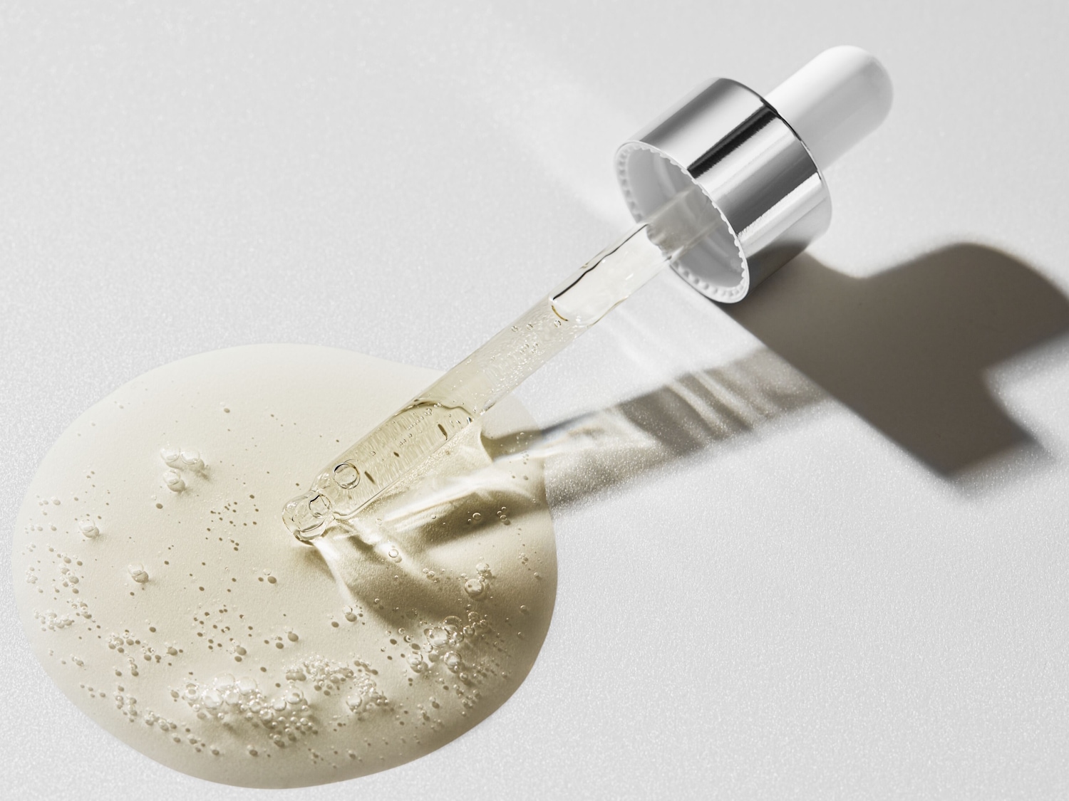 Kropla serum z pipetą na białym tle, ukazująca jego lekką, płynną konsystencję.