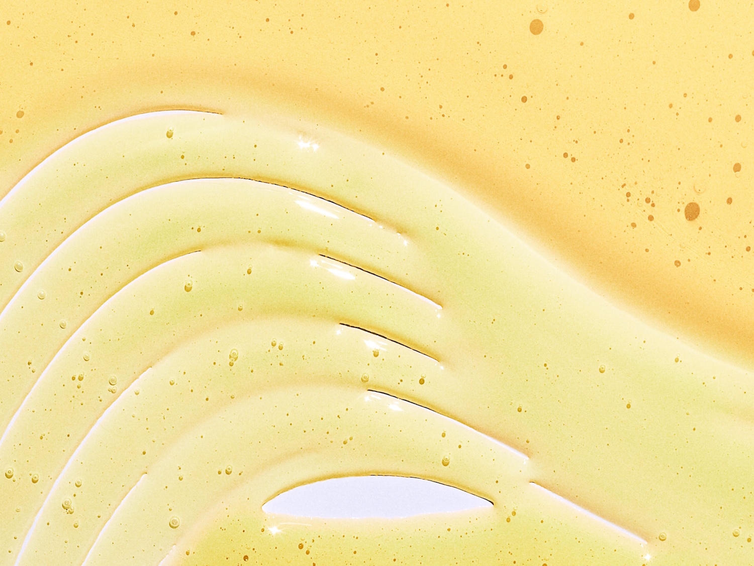 Primer plano de un suero facial dorado y brillante, extendido en ondas suaves, revelando una textura rica y nutritiva.