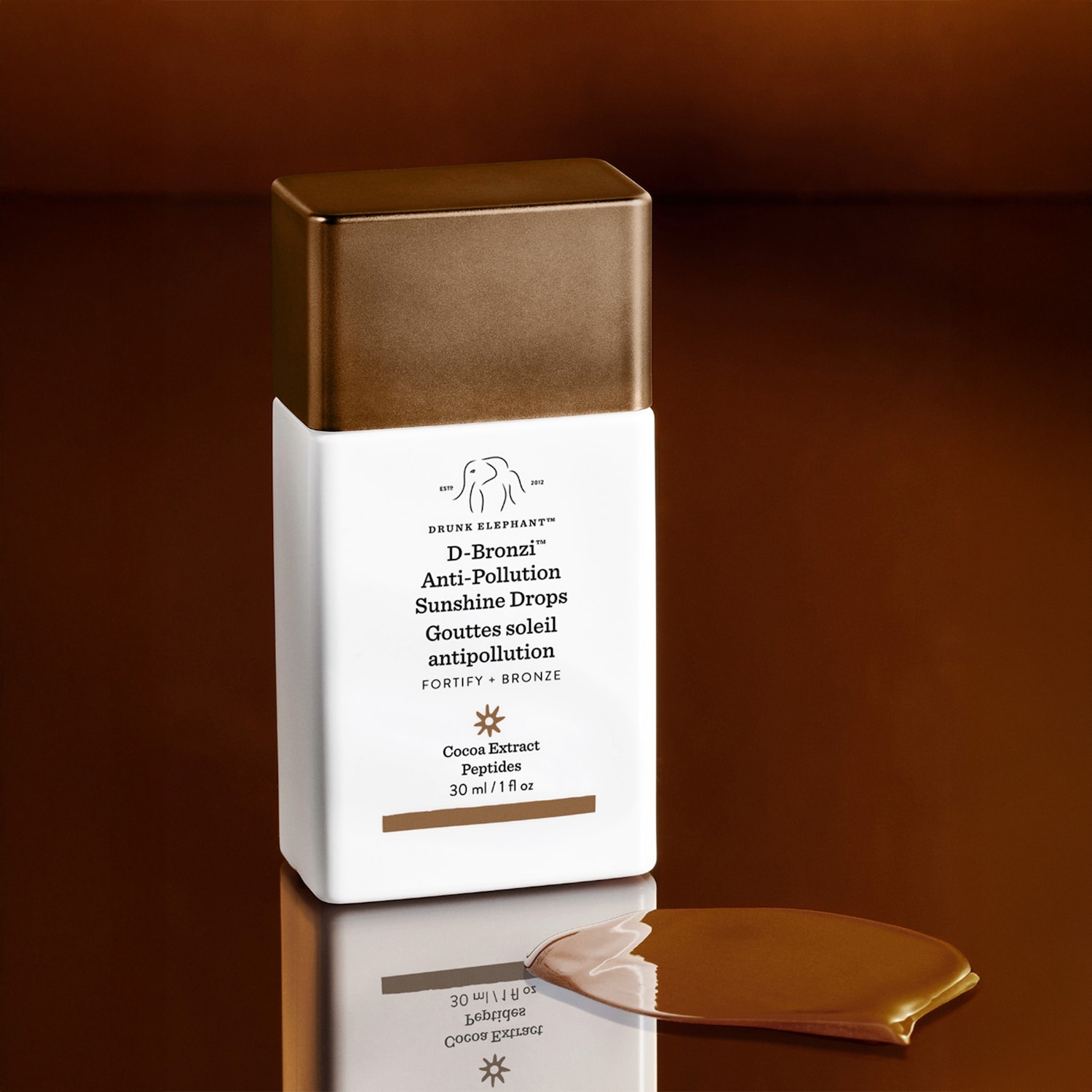 Drunk Elephant D-Bronzi Anti-Pollution Sunshine Drops in een witte fles met een bronzen dop, naast een plasje van het product om de kleur te laten zien.