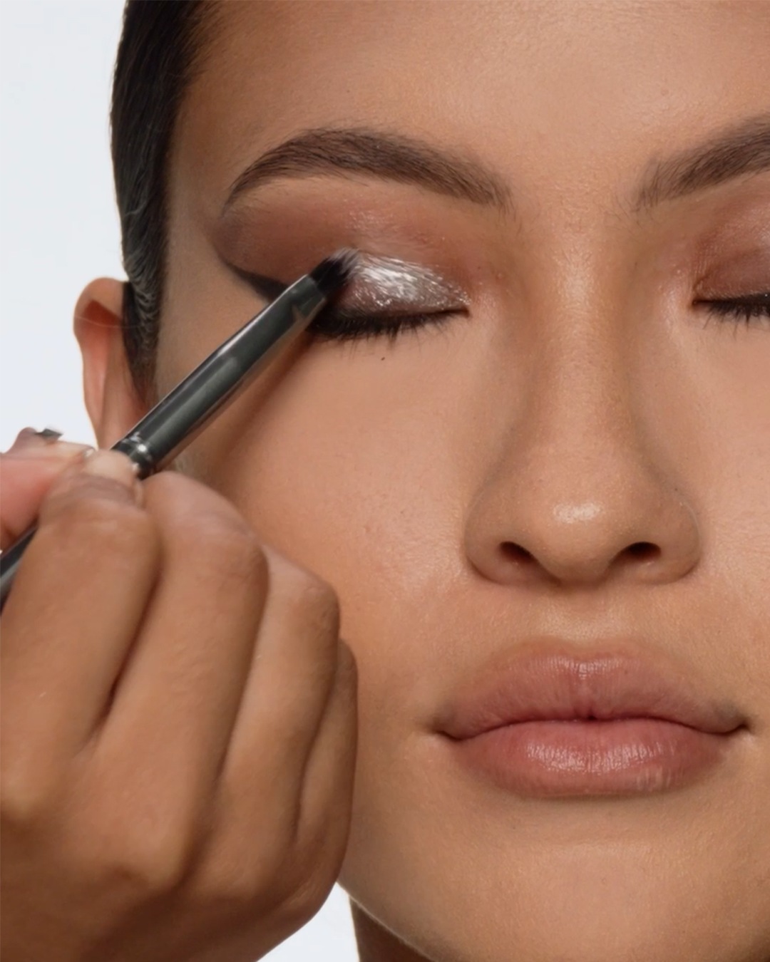 Een make-up artist brengt met een zilveren kwast glinsterende oogschaduw aan op het ooglid van een vrouw, voor een stralende en verfijnde look.