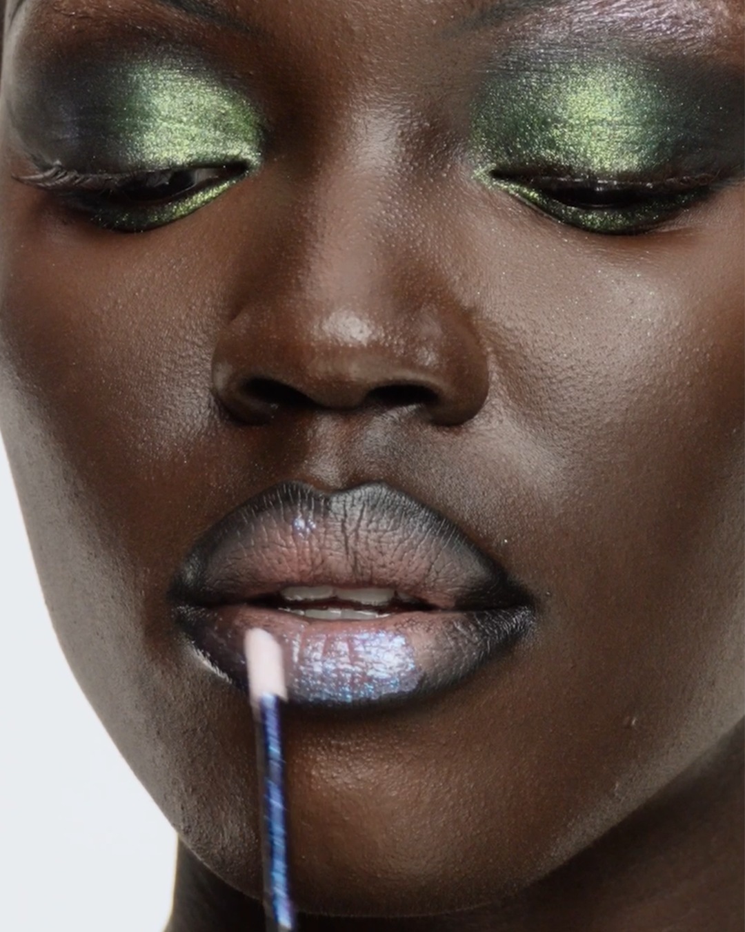 Close-up van een vrouw met groene oogschaduw en glanzende lippenstift die wordt aangebracht met een blauwe applicator.