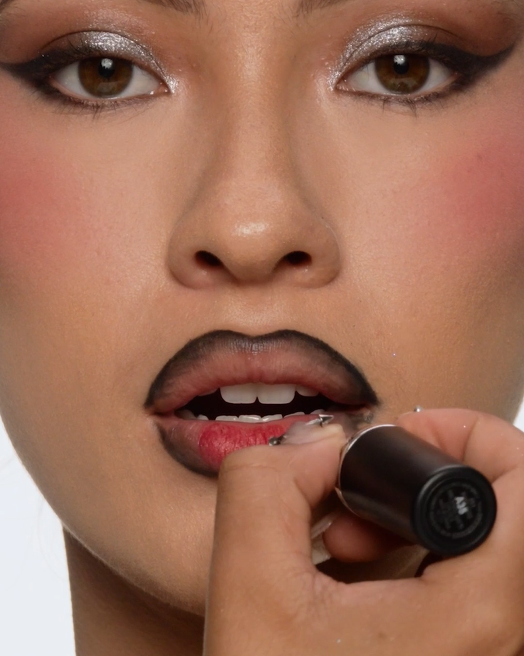 Een vrouw brengt zwarte lippenstift aan, met een gedurfde zwarte omlijning en zilveren oogschaduw, voor een opvallende make-uplook.