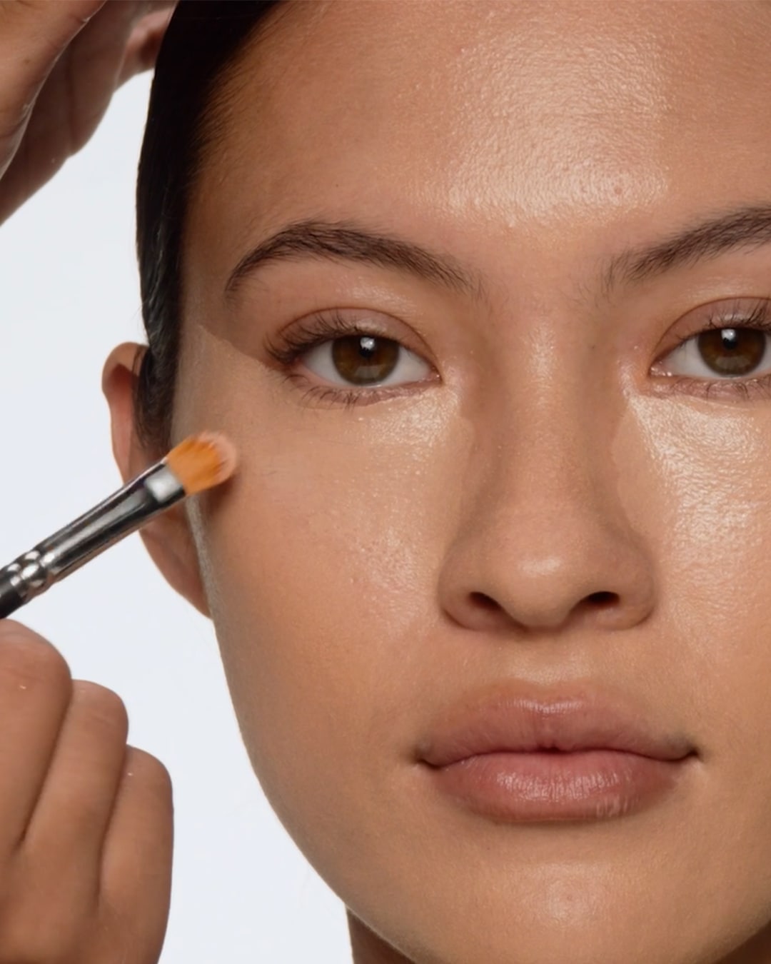 Een make-up artist brengt met een penseel concealer aan onder het oog van een model om de huid te egaliseren.