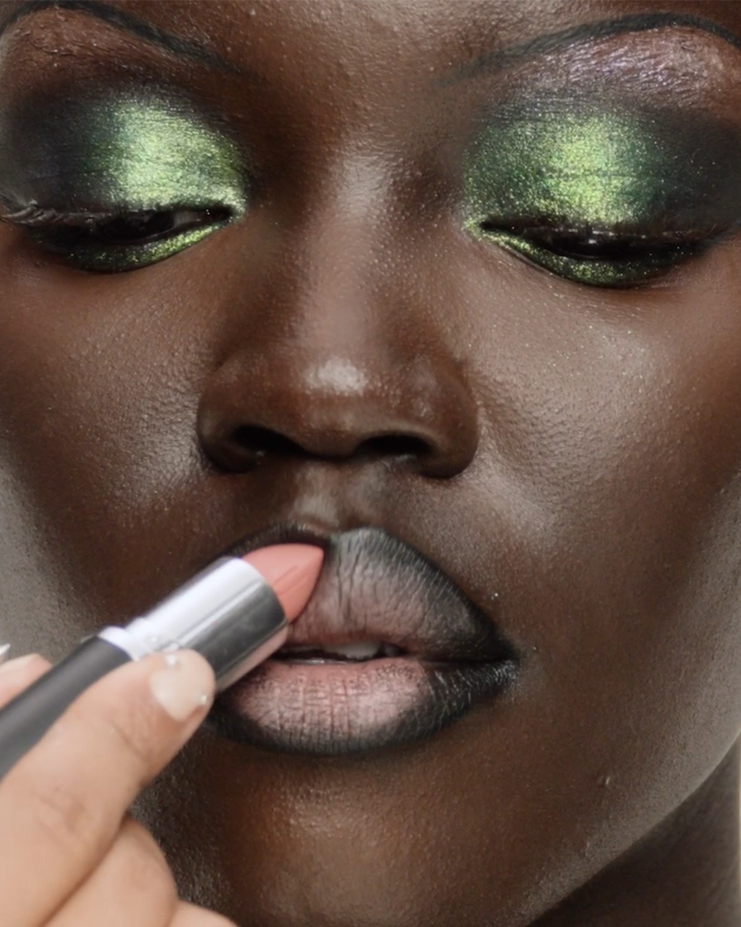 Een close-up van een vrouw met groene oogschaduw en een perzikkleurige lippenstift die op haar lippen wordt aangebracht.