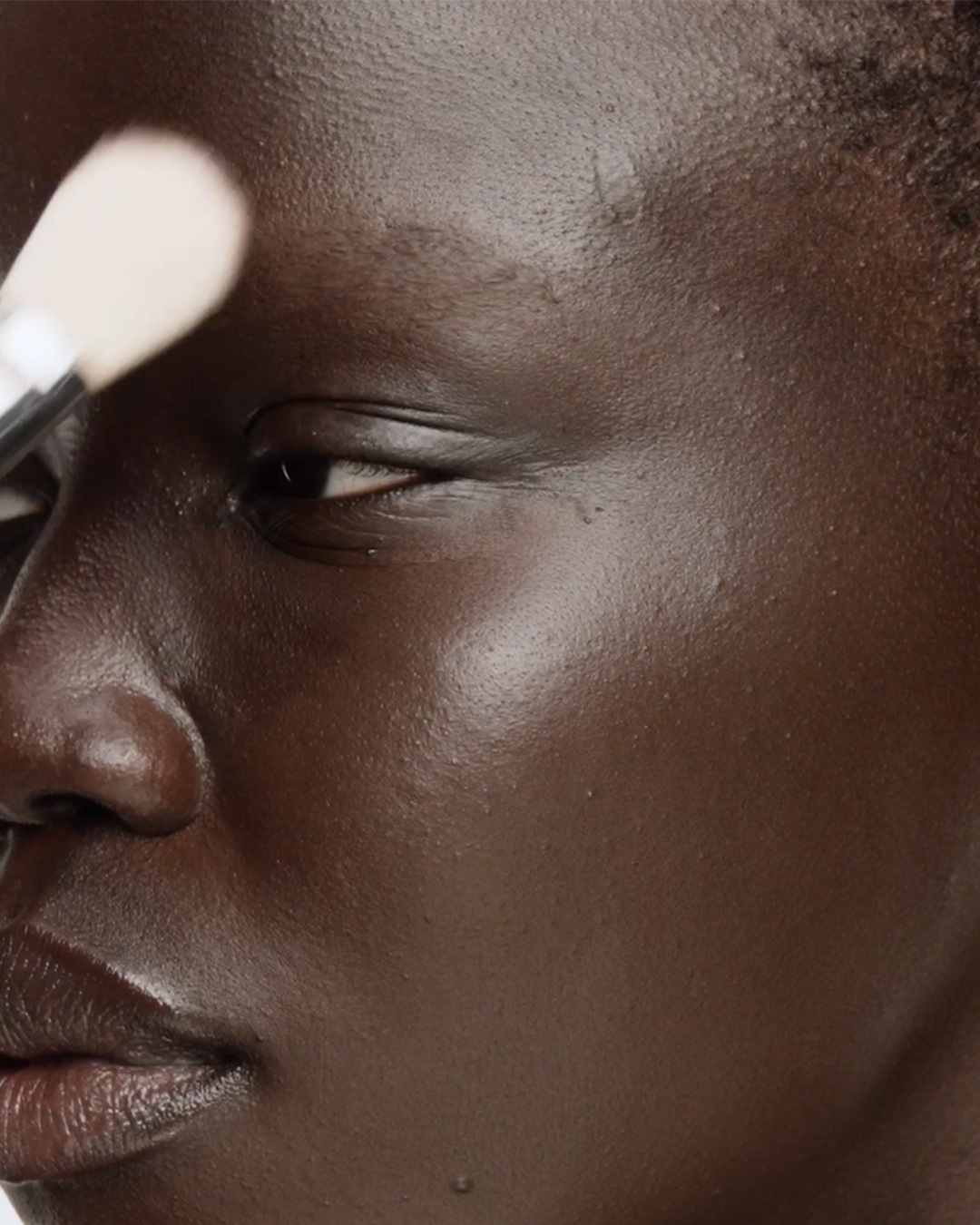 Close-up van een donkere huid die wordt gepoederd met een make-upborstel voor een egale en stralende teint.