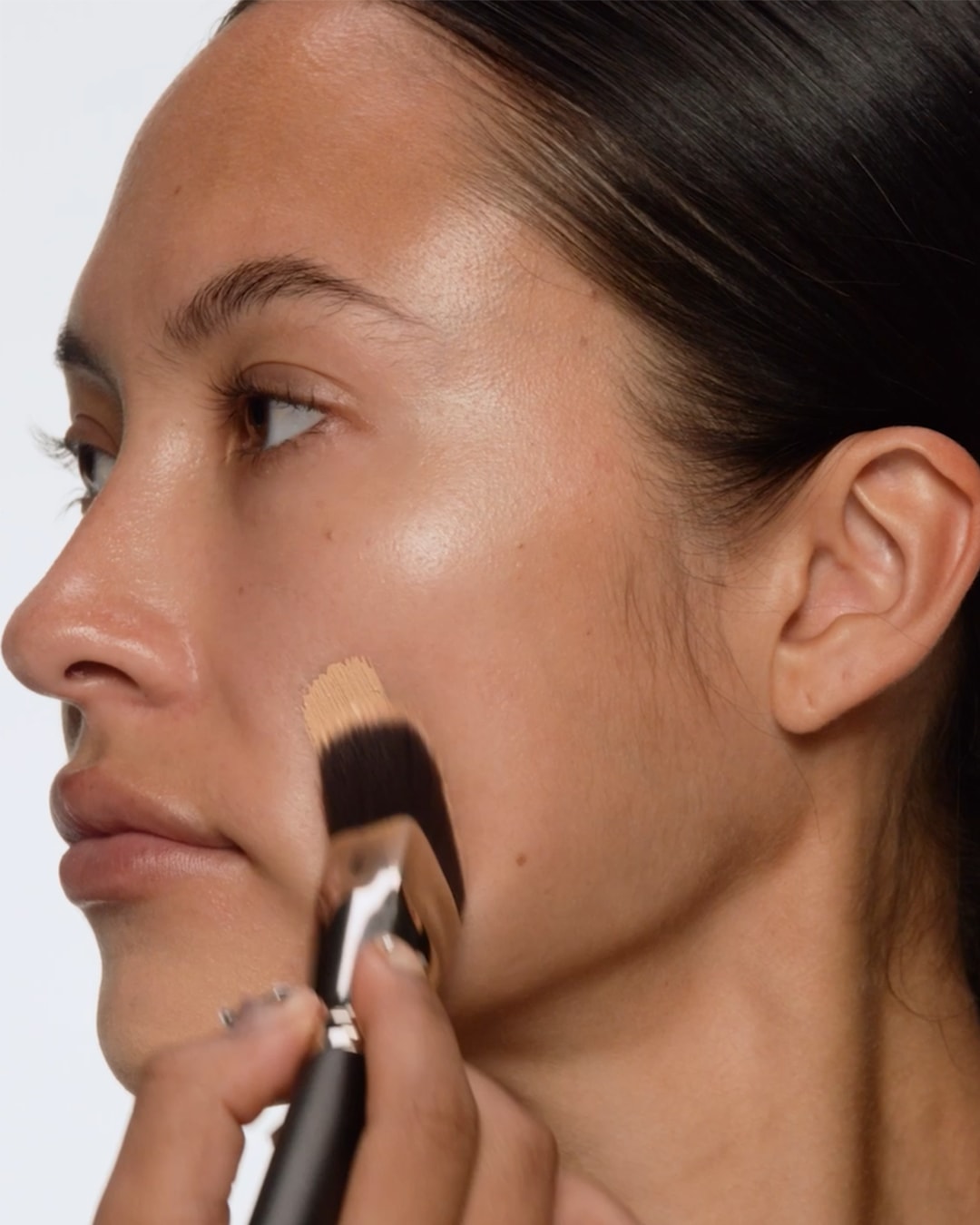 Een vrouw brengt foundation aan met een make-upborstel voor een egale teint.