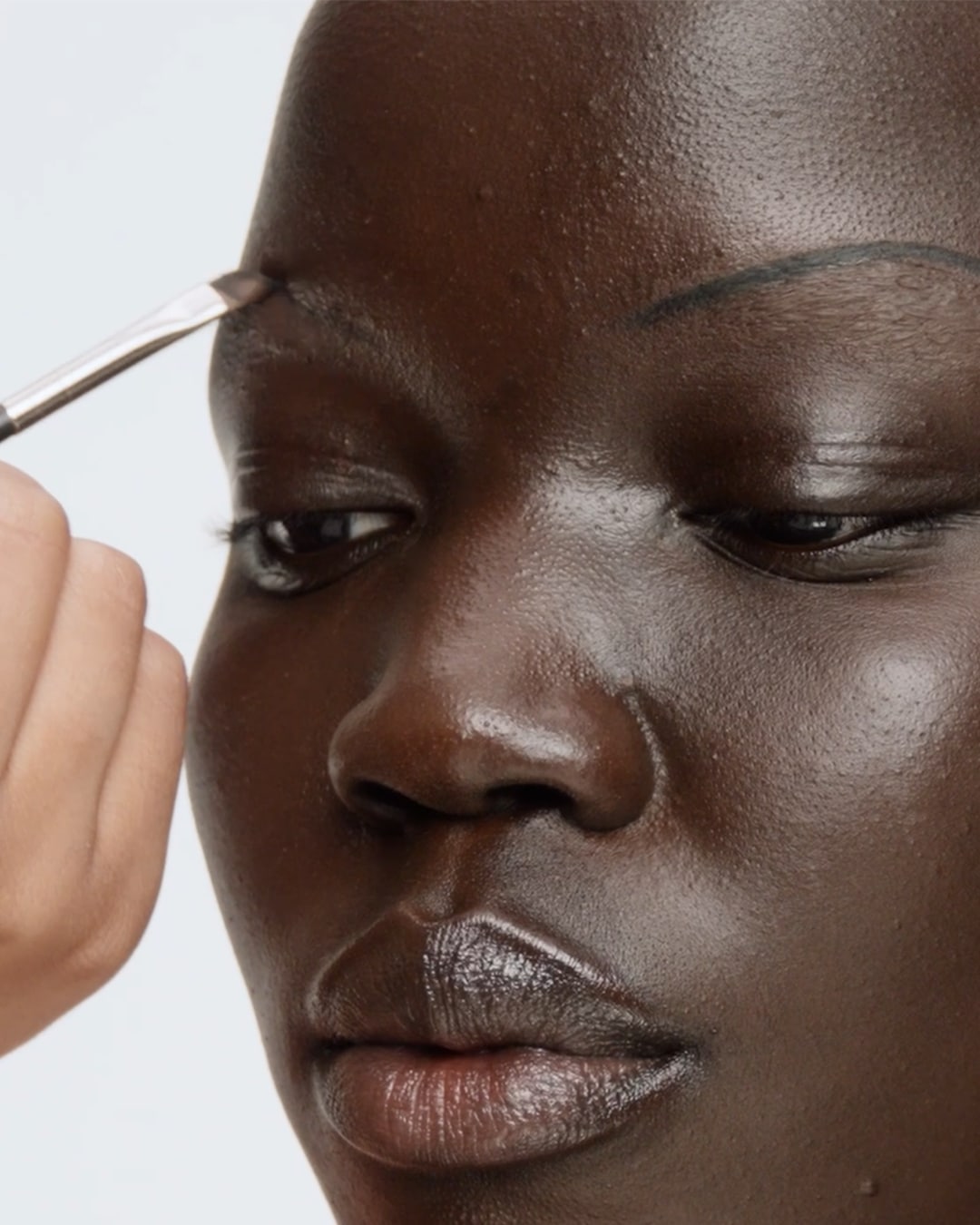 Close-up van een vrouw met een donkere huid die make-up op haar wenkbrauwen aanbrengt met een borstel.