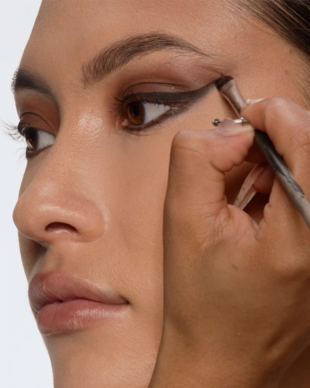 Een close-up van een vrouw die zwarte eyeliner aanbrengt met een penseel om een strakke, gevleugelde look te creëren.