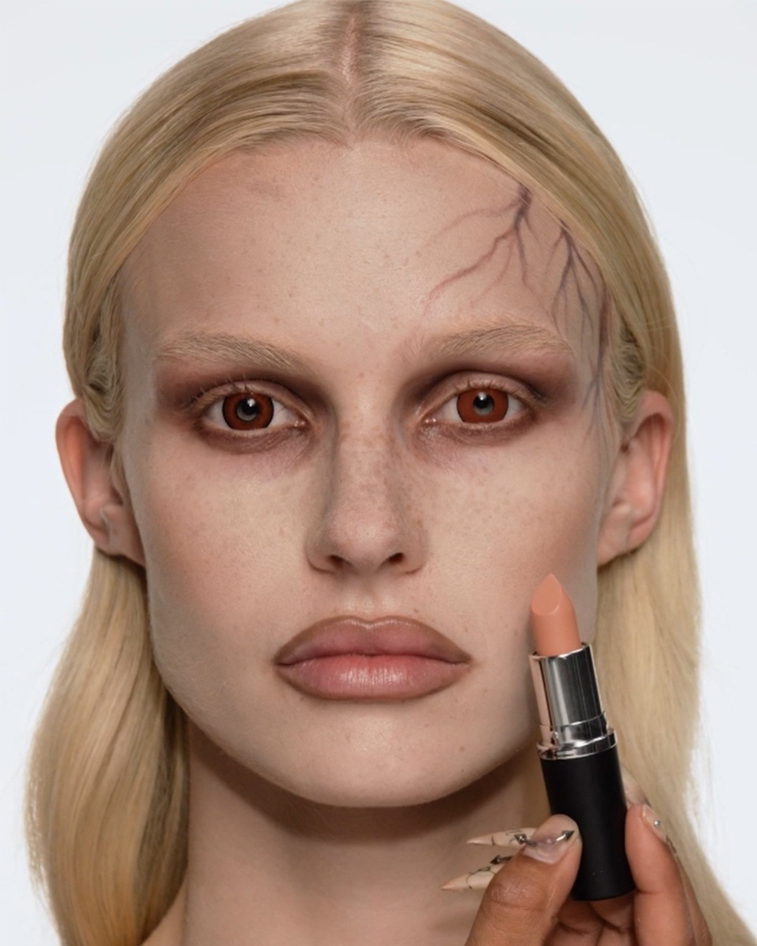 Een vrouw met blond haar en bruine ogen houdt een perzikkleurige lippenstift vast, klaar om haar lippen te accentueren voor een perfecte make-up look.