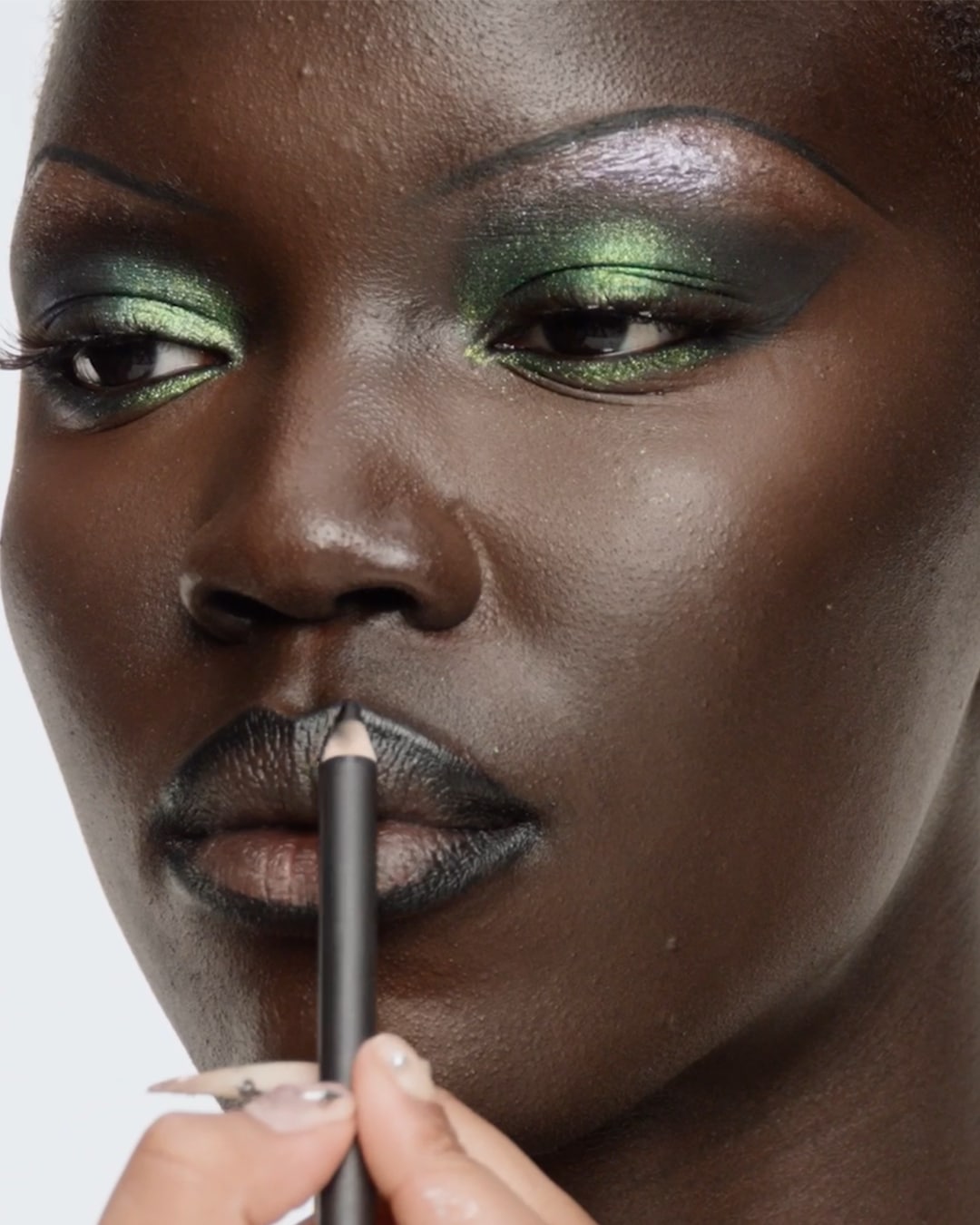 Een vrouw met een donkere huidskleur brengt zwarte lipliner aan, met groene oogschaduw die haar ogen accentueert.