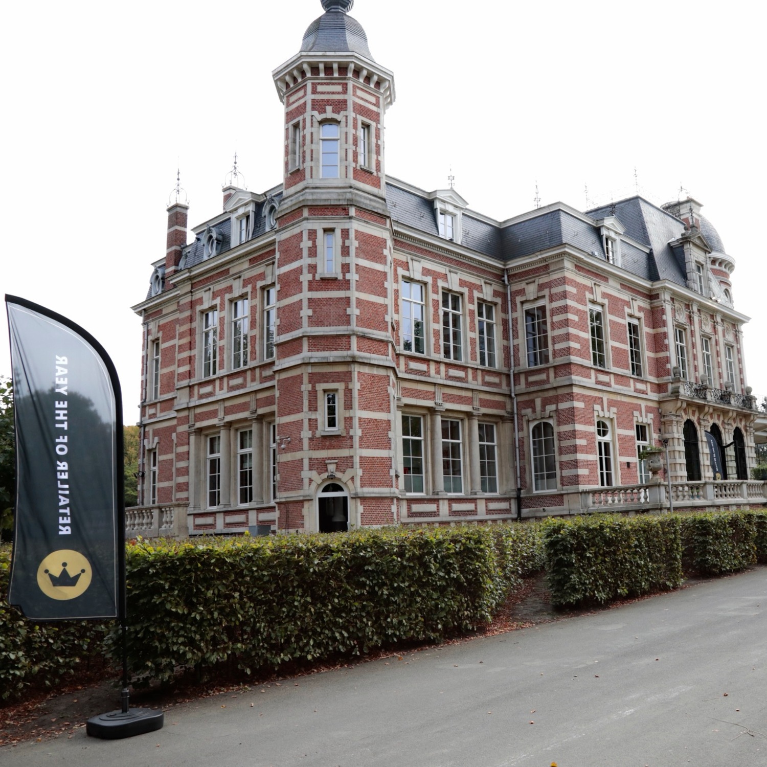 Voici un grand bâtiment de trois étages en briques rouges et blanches, avec un drapeau noir portant une couronne dorée sur le côté gauche.