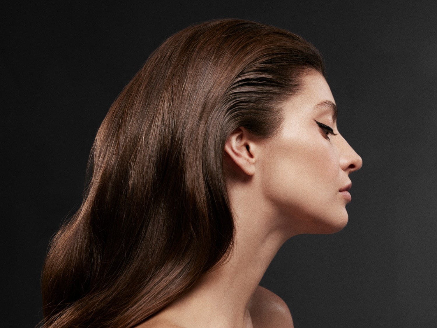 Profiel van een vrouw met bruin haar en zwarte eyeliner, die een elegante en verfijnde uitstraling creëert.