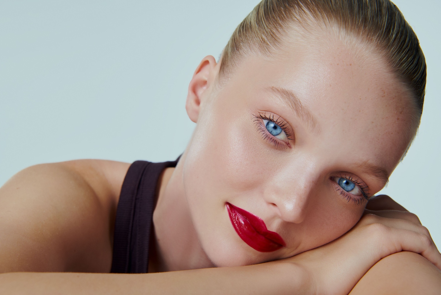Nahaufnahme einer Frau mit strahlend blauen Augen und glänzend roten Lippen, die auf ihren Armen ruht.