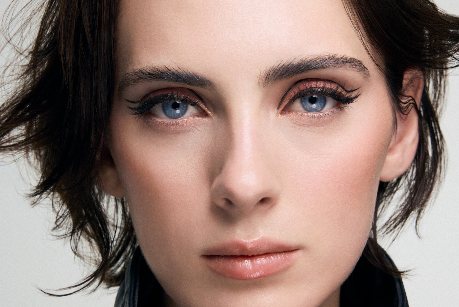 Nahaufnahme eines Frauengesichts mit strahlend blauen Augen, betont durch einen feinen, schwarzen Eyeliner und zarte, rosafarbene Lidschatten, die den Blick verführerisch hervorheben.