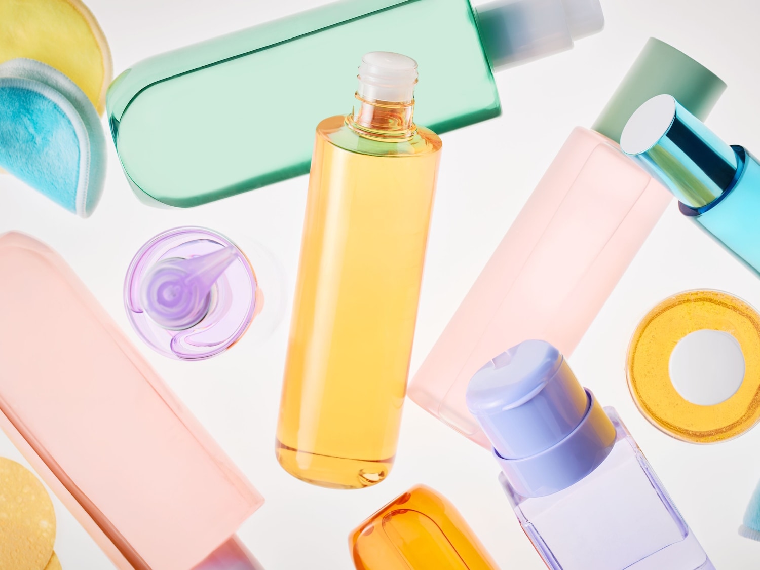 Variedad de productos de belleza en envases de colores pastel como rosa, verde, amarillo y azul, incluyendo tónicos, limpiadores y discos desmaquillantes.