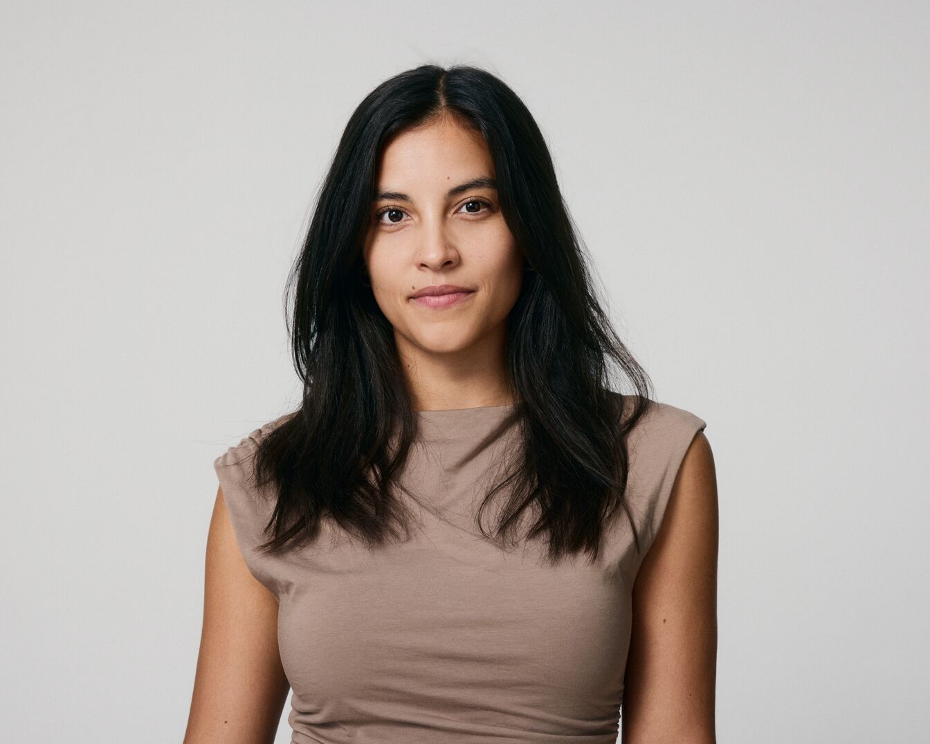 Eine Frau mit langen, dunklen Haaren und einem hellbraunen Oberteil blickt direkt in die Kamera.