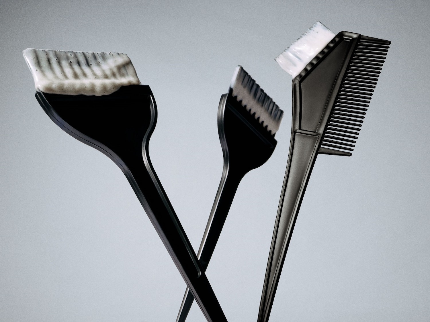 Ecco tre pennelli neri per la tinta dei capelli, uno con setole imbevute di crema bianca, perfetti per un'applicazione precisa e uniforme.