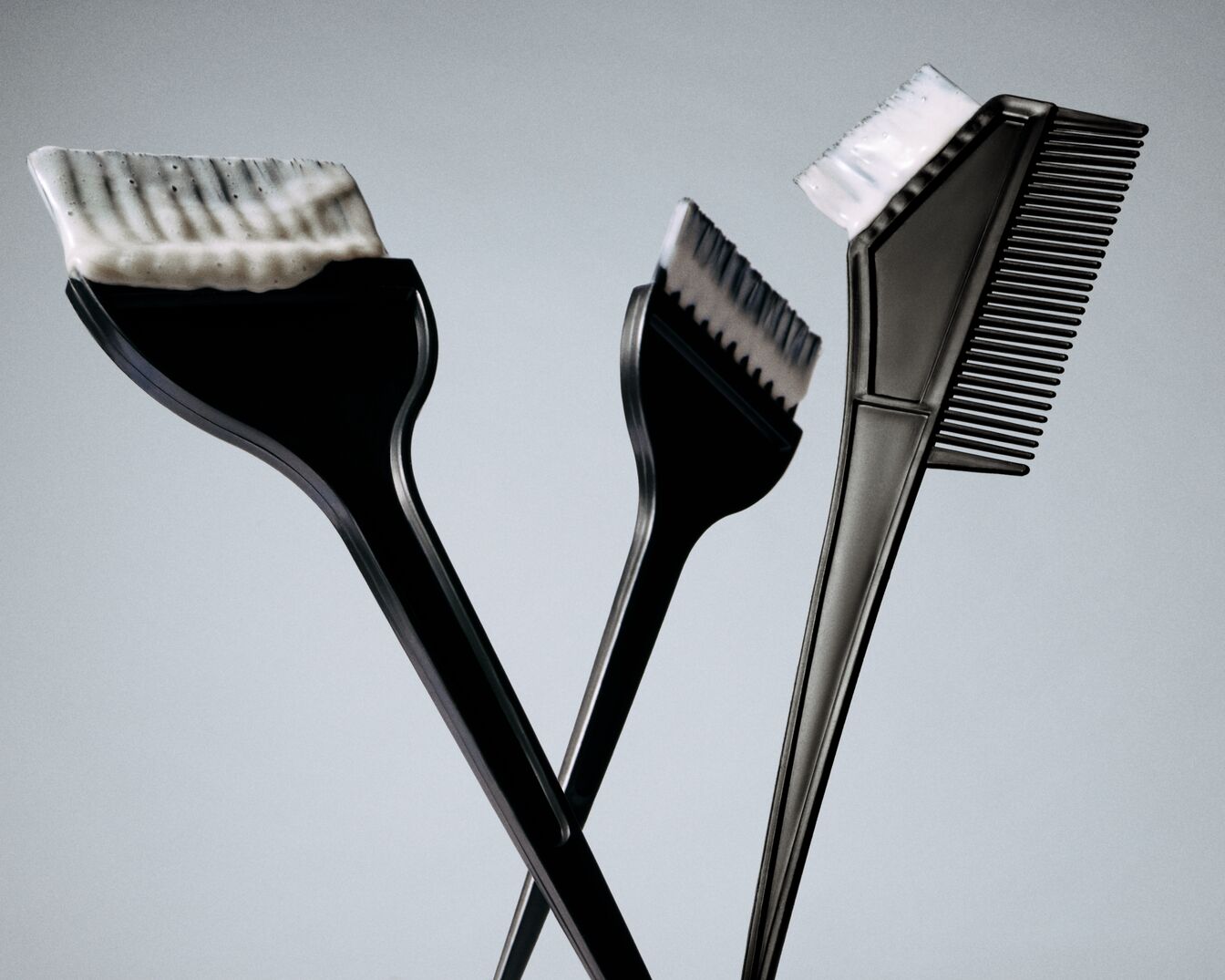 Ecco tre pennelli neri per la colorazione dei capelli, uno con setole imbiancate dalla crema colorante, pronti a trasformare il tuo look.