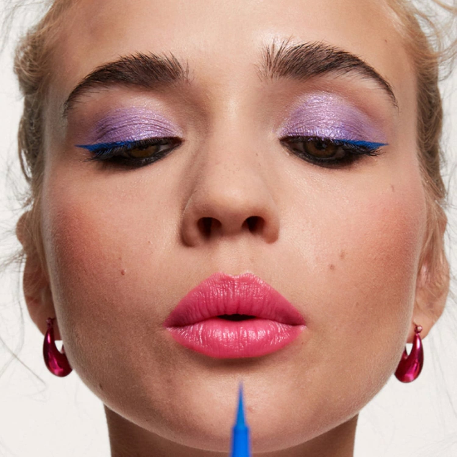 Nahaufnahme eines Gesichts mit lila Lidschatten, blauem Eyeliner und pinkfarbenen Lippen.