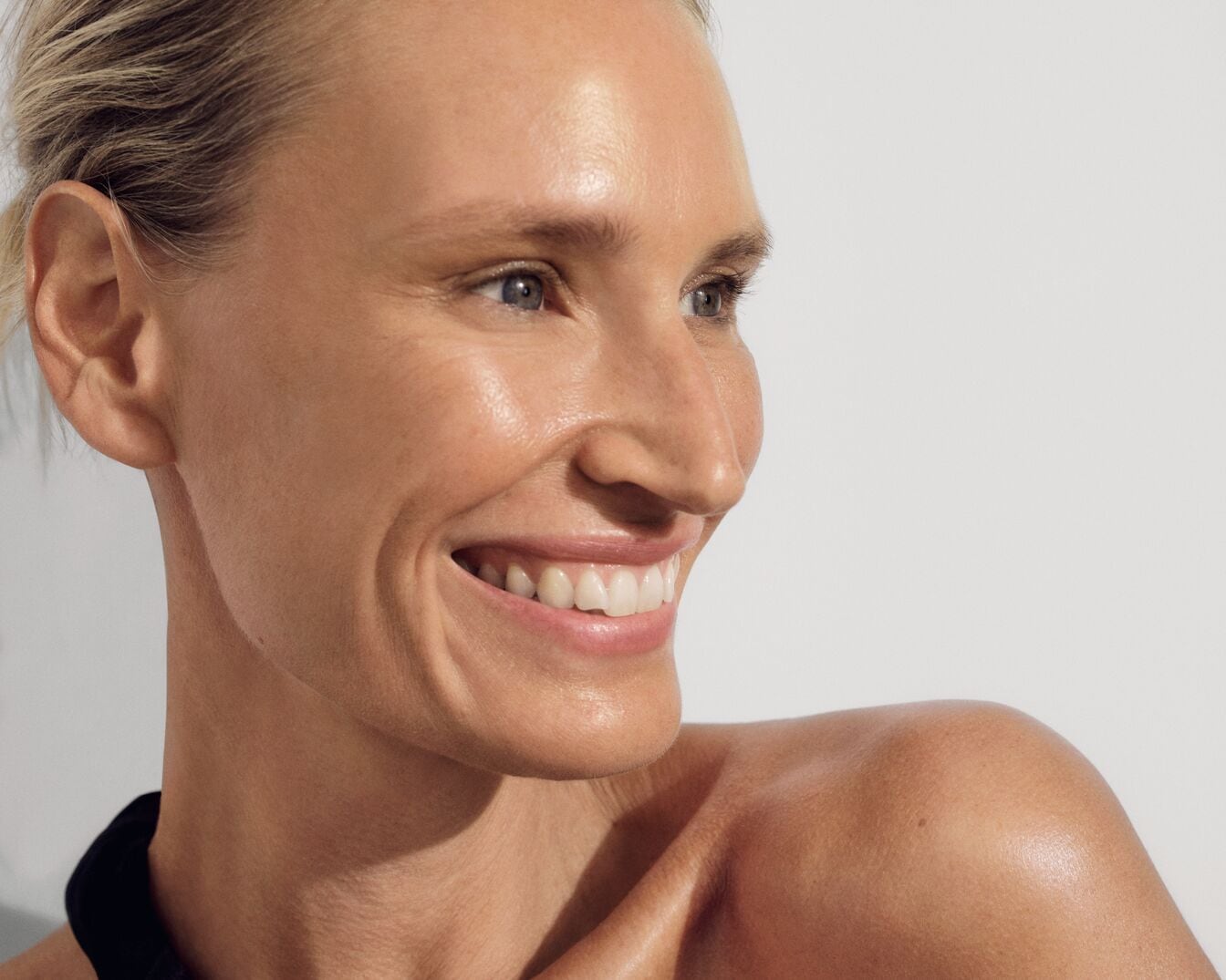 Primo piano di una donna bionda sorridente con la pelle luminosa e un top nero, che mostra un aspetto sano e radioso.