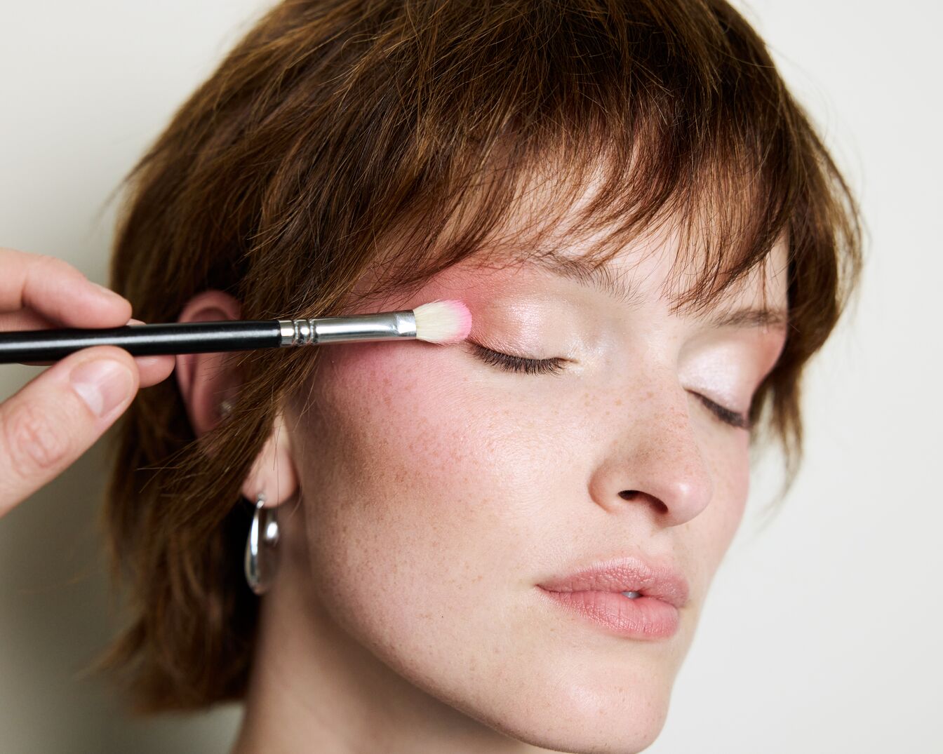 Na powiece kobiety pędzelkiem nakładany jest różowy cień do powiek, tworząc subtelny, promienny wygląd.