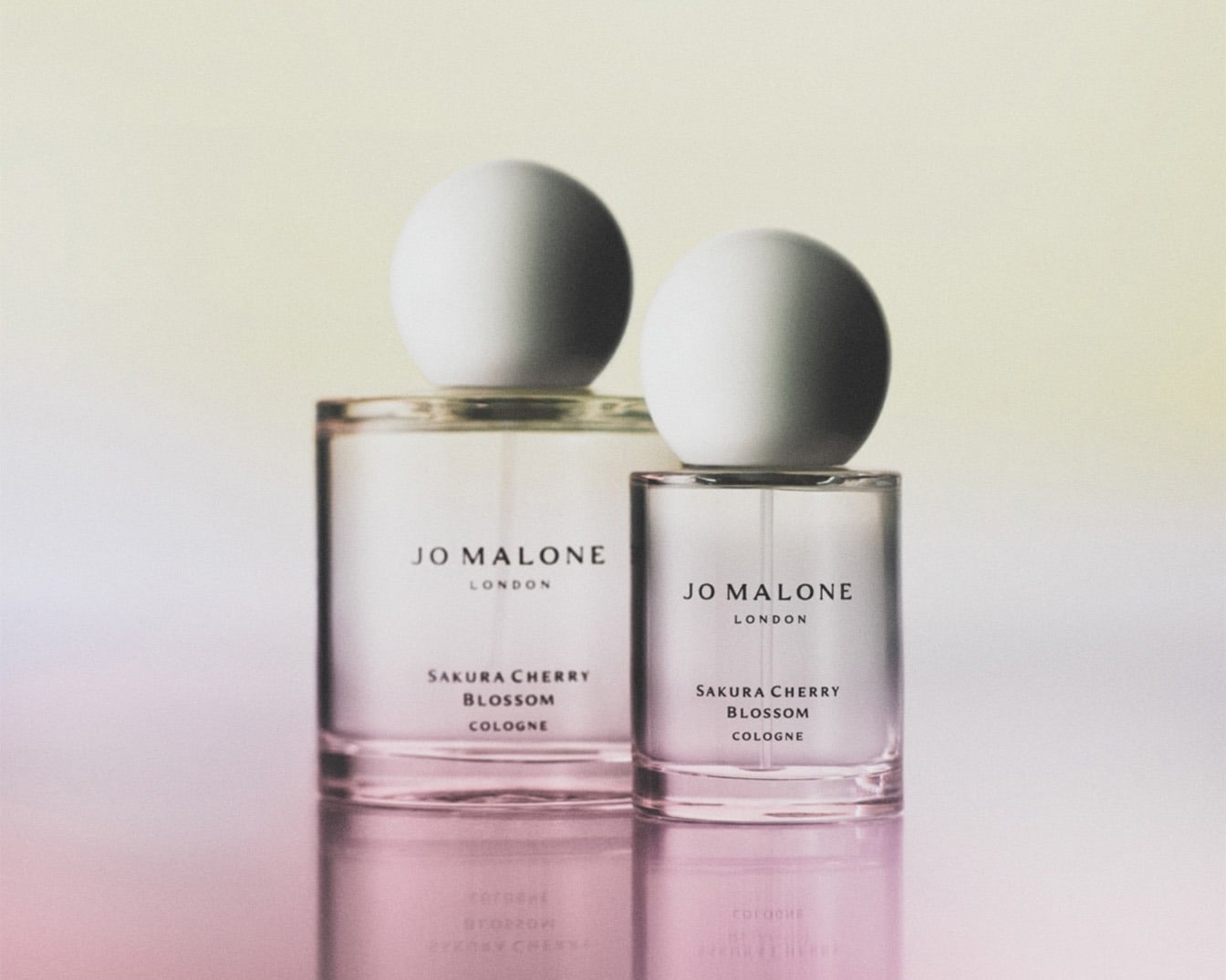 Twee heldere glazen flessen Jo Malone Sakura Cherry Blossom Cologne met witte bolvormige doppen staan op een glanzend oppervlak.