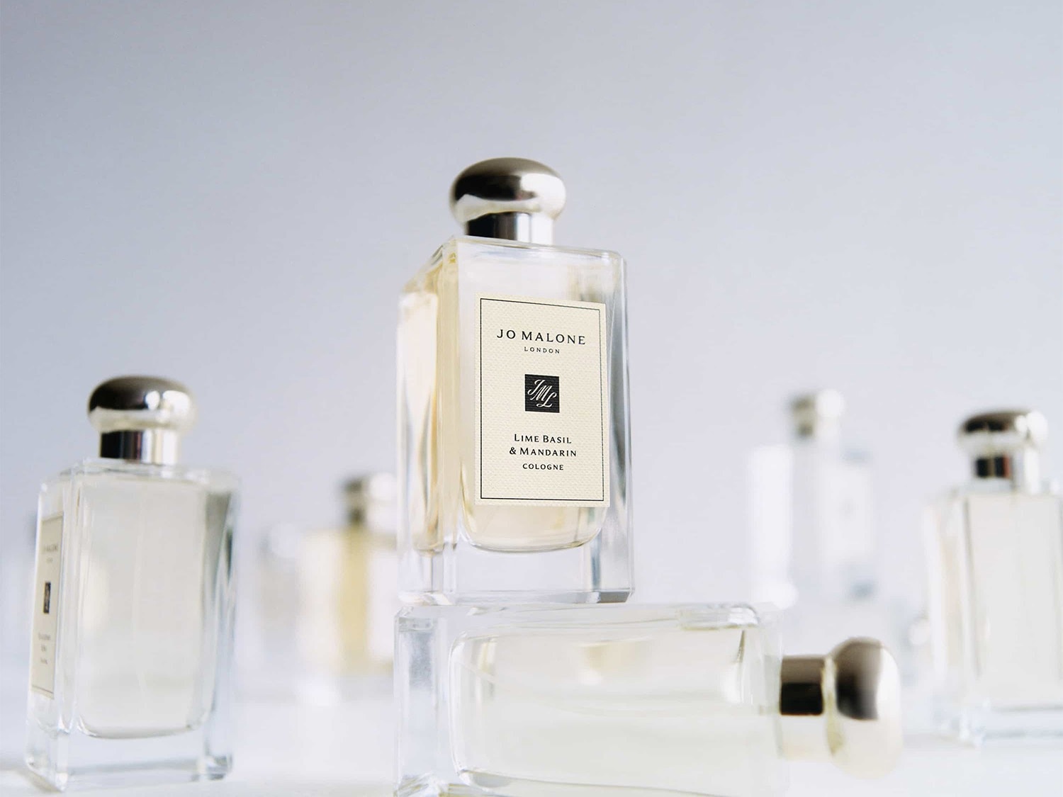 De Jo Malone London Lime Basil & Mandarin Cologne in een heldere glazen fles met een zilveren dop, gestapeld op andere flessen, straalt een frisse en verfijnde geur uit.