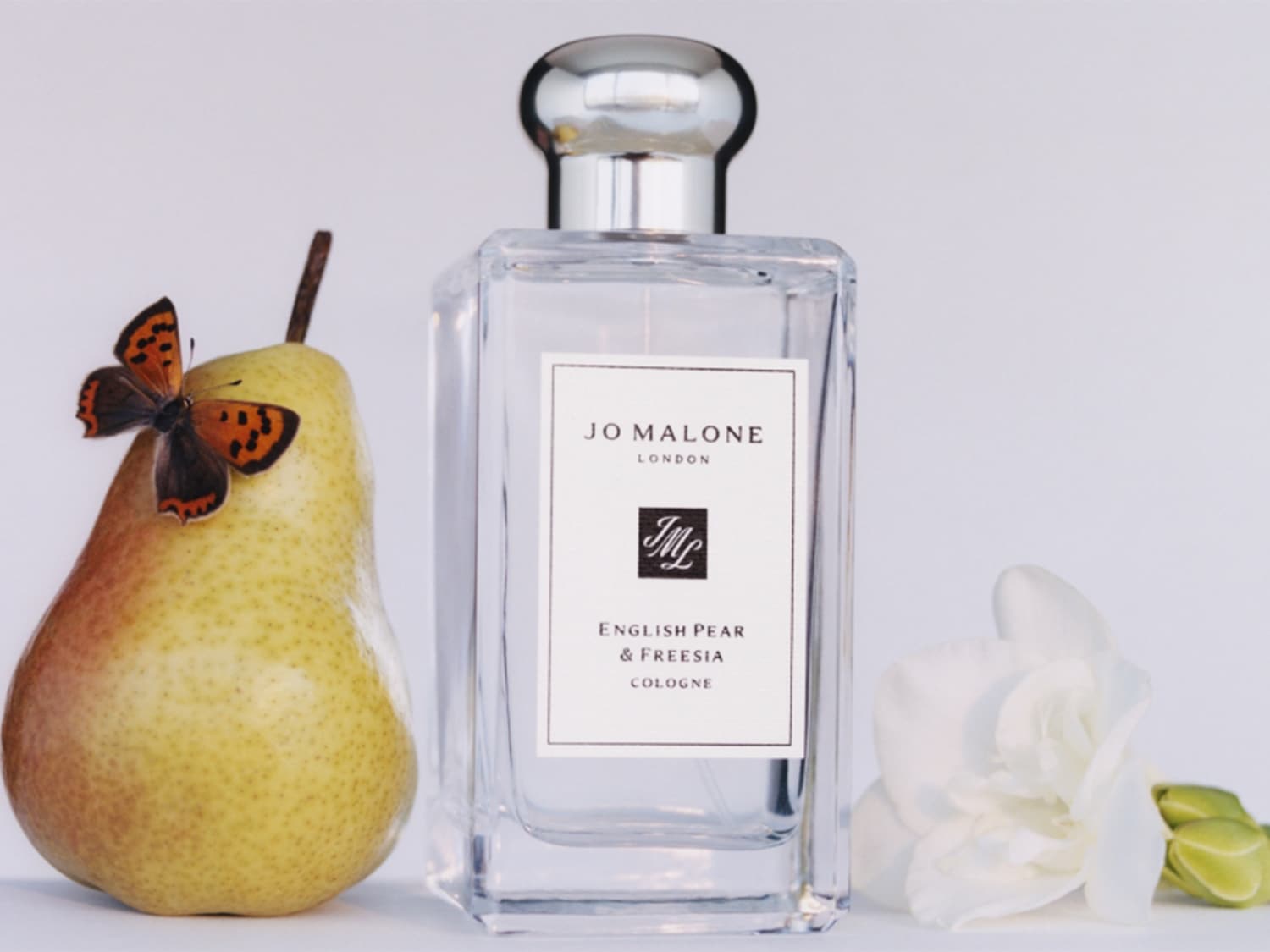 Une voiture beige transporte des poires géantes et un parfum Jo Malone sur son toit, évoquant un voyage olfactif fruité et luxueux.