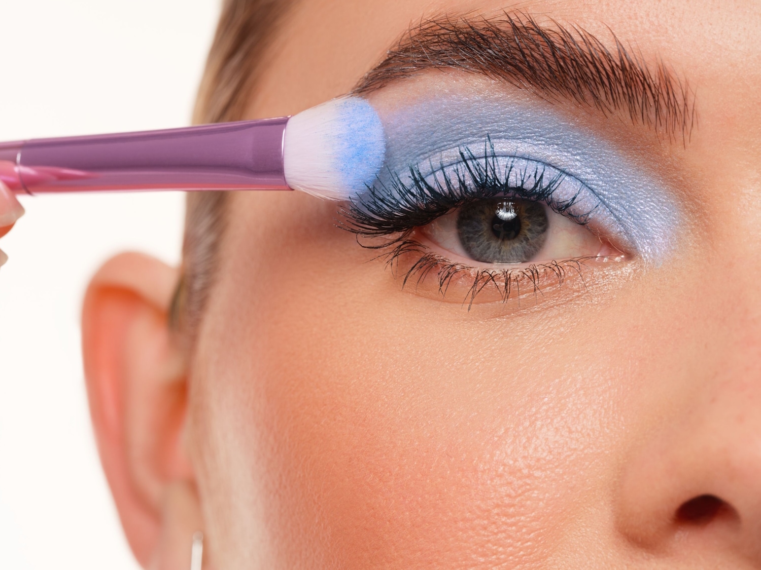 Con un pincel de mango morado, se aplica sombra de ojos azul brillante en el párpado para un look llamativo.