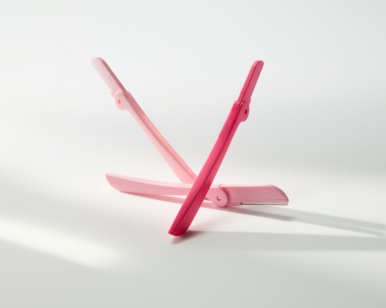 Twee roze wenkbrauwtrimmers, één lichtroze en één felroze, gekruist op een witte achtergrond.