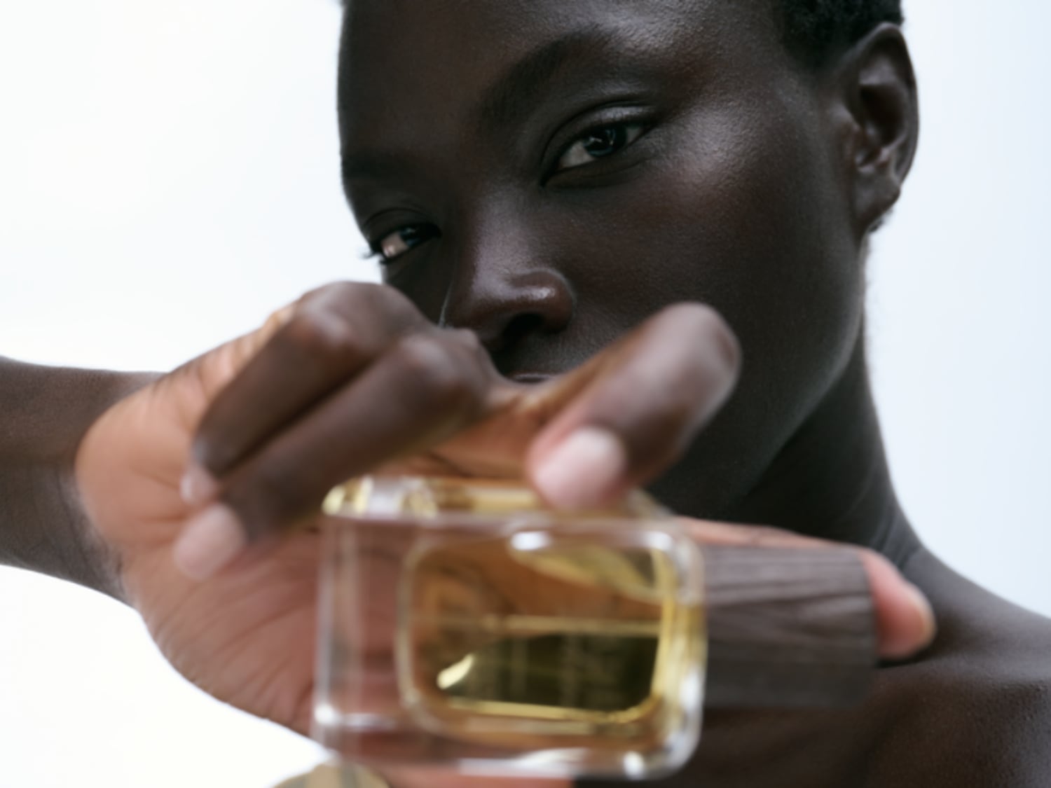 Una persona de piel oscura sostiene un frasco de perfume dorado, resaltando su elegancia y sofisticación.