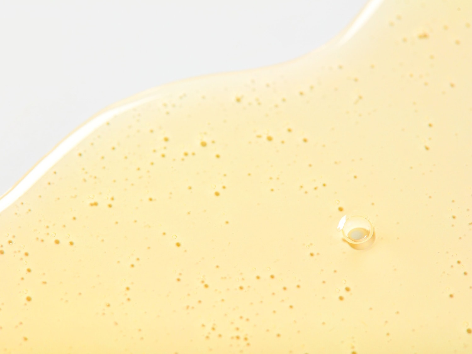 Primer plano de un fluido viscoso de color amarillo claro con pequeñas burbujas, que muestra su textura y consistencia.