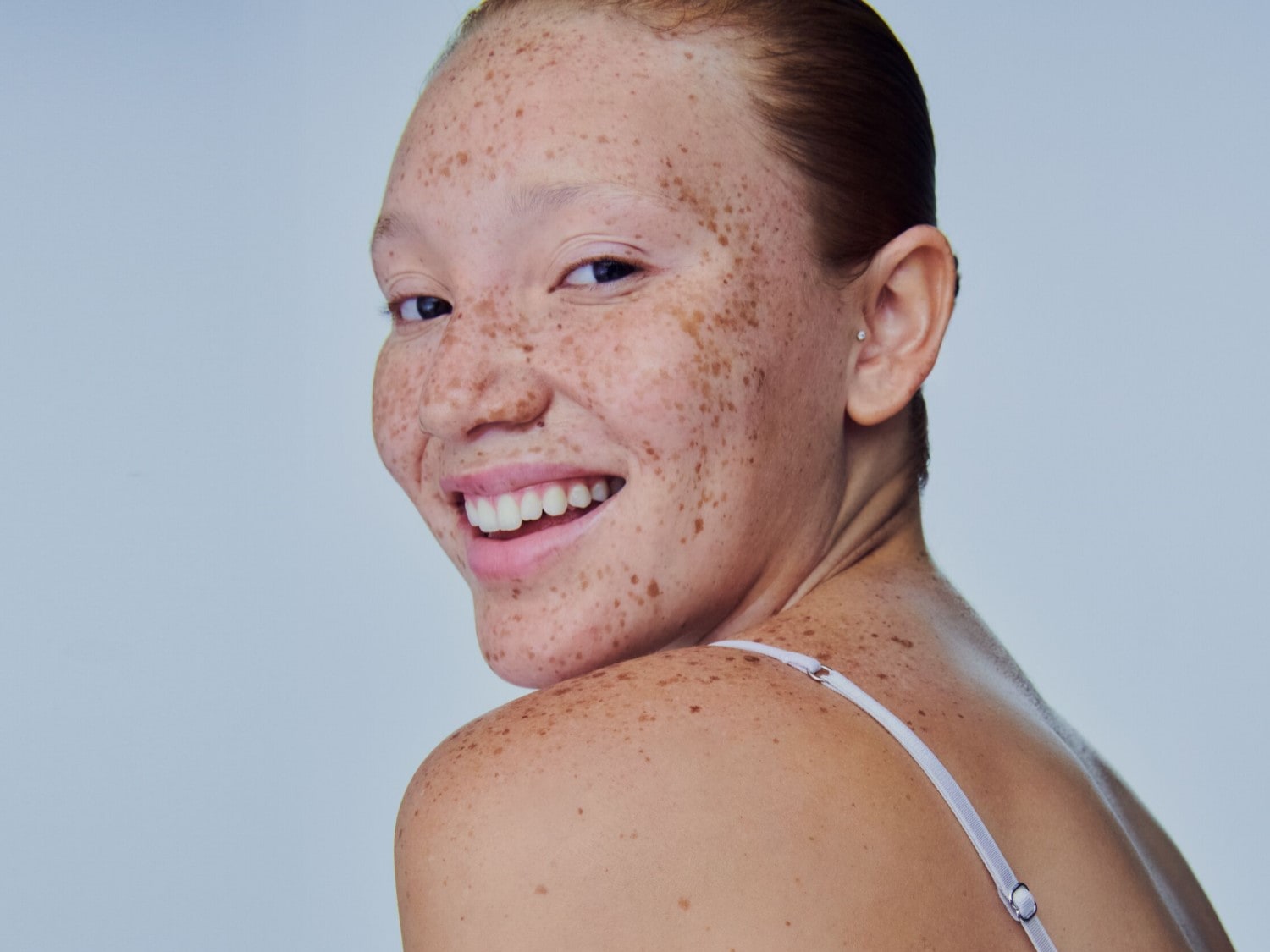 Una mujer sonriente con pecas y cabello rojizo, mirando por encima del hombro con una expresión alegre.