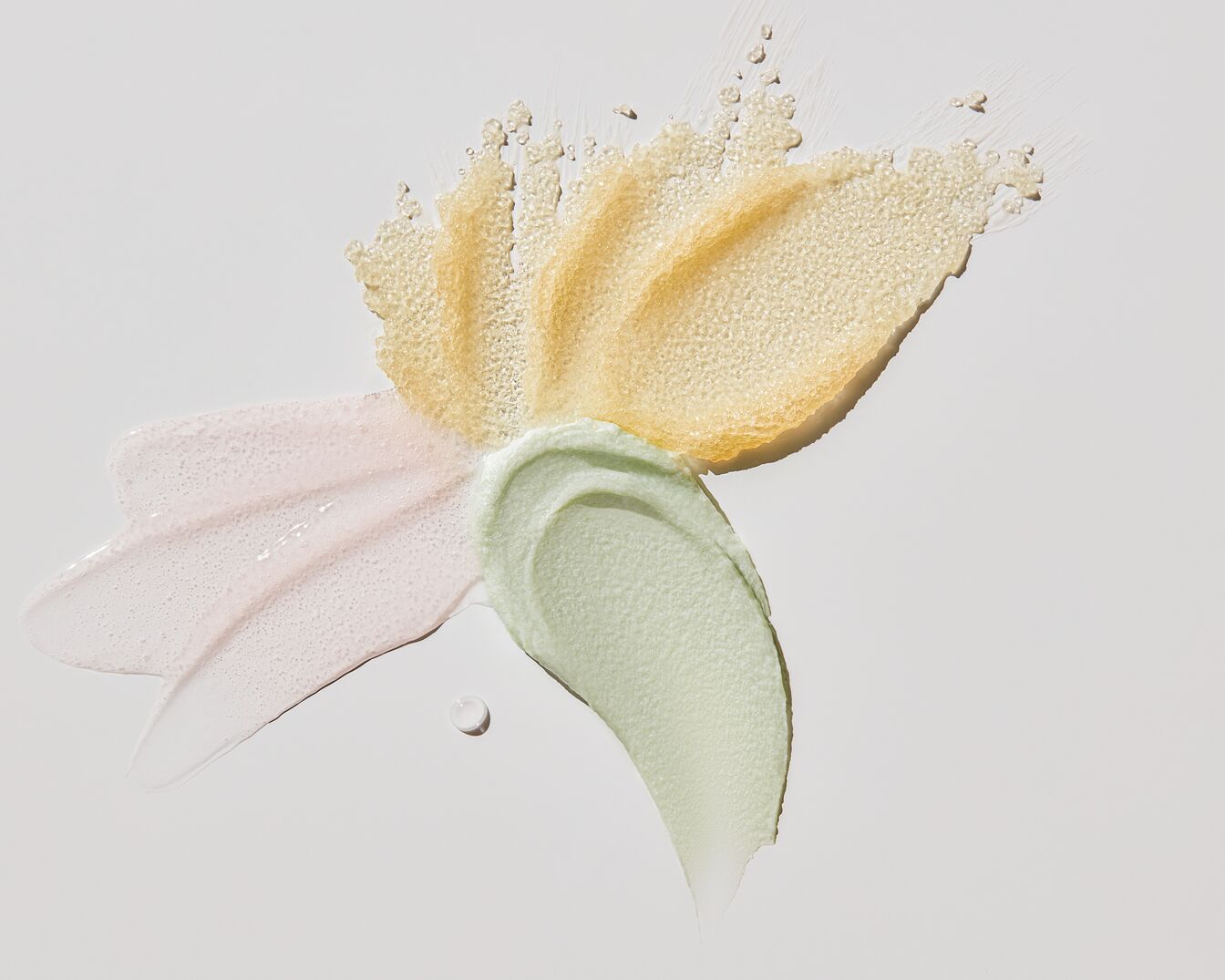 Ecco degli swatch di prodotti di bellezza: uno scrub dorato, una crema rosa chiaro e una crema verde chiaro, perfetti per la cura della pelle.