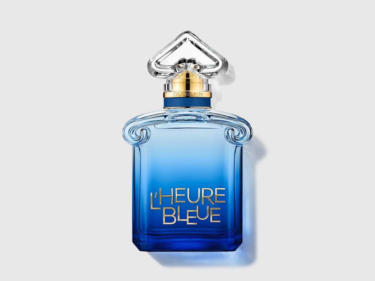 Le parfum L'Heure Bleue de Guerlain est présenté dans un flacon en verre bleu dégradé, orné d'un bouchon argenté et doré, avec le nom du parfum écrit en lettres dorées sur le devant.