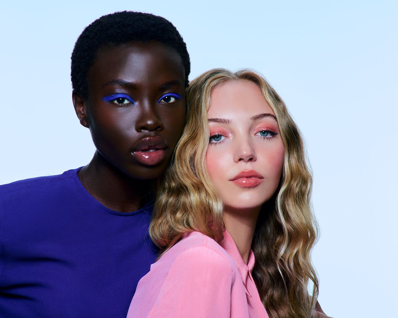 Zwei Models mit auffälligem Augen-Make-up: Eine mit blauem Eyeliner und Schwarzer Haut, die andere mit rosa Lidschatten und blonden, gewellten Haaren.