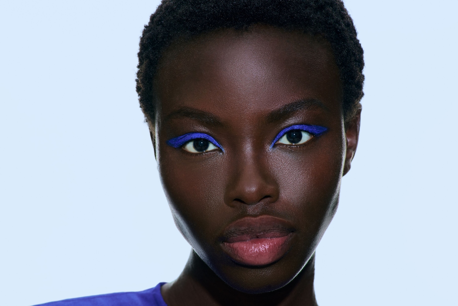 Nahaufnahme eines Schwarzen Models mit einem präzisen, leuchtend blauen Eyeliner, der ihre Augen betont.