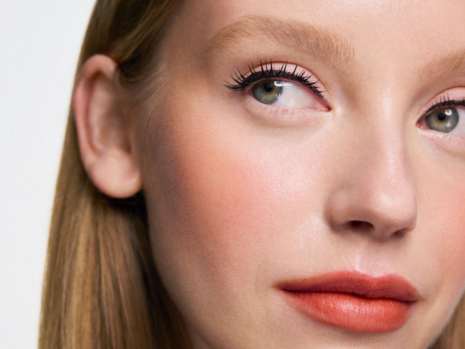 Nahaufnahme eines Frauengesichts mit natürlichem Make-up, das einen orangefarbenen Lippenstift und getuschte Wimpern hervorhebt.