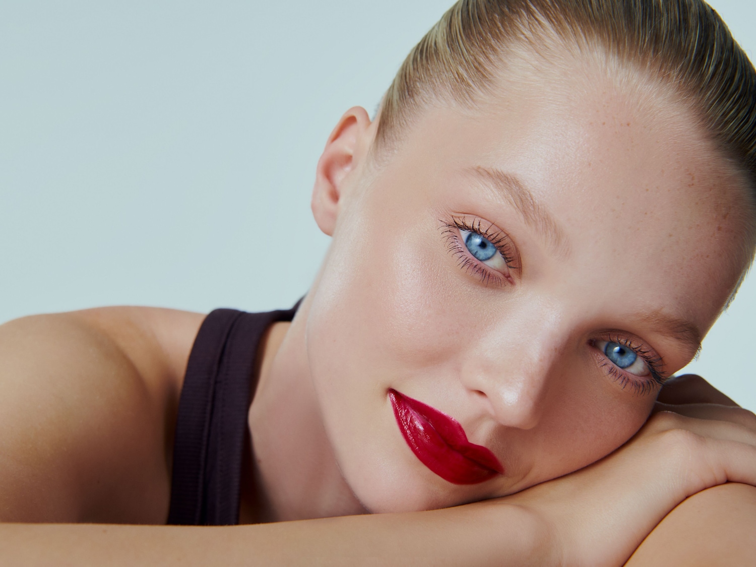 Nahaufnahme einer Frau mit strahlend blauen Augen und glänzend roten Lippen, die auf ihren verschränkten Armen ruht.