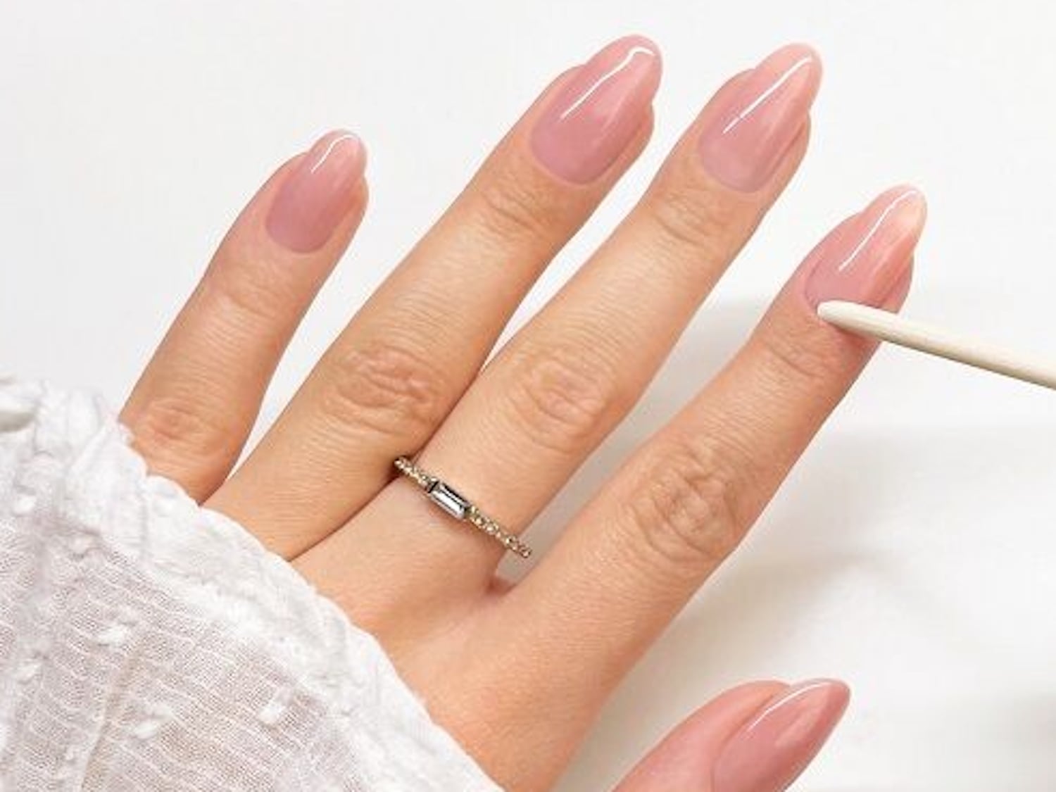 Nahaufnahme einer Hand mit mandelförmigen, glänzend rosa lackierten Nägeln und einem goldenen Ring am Finger.