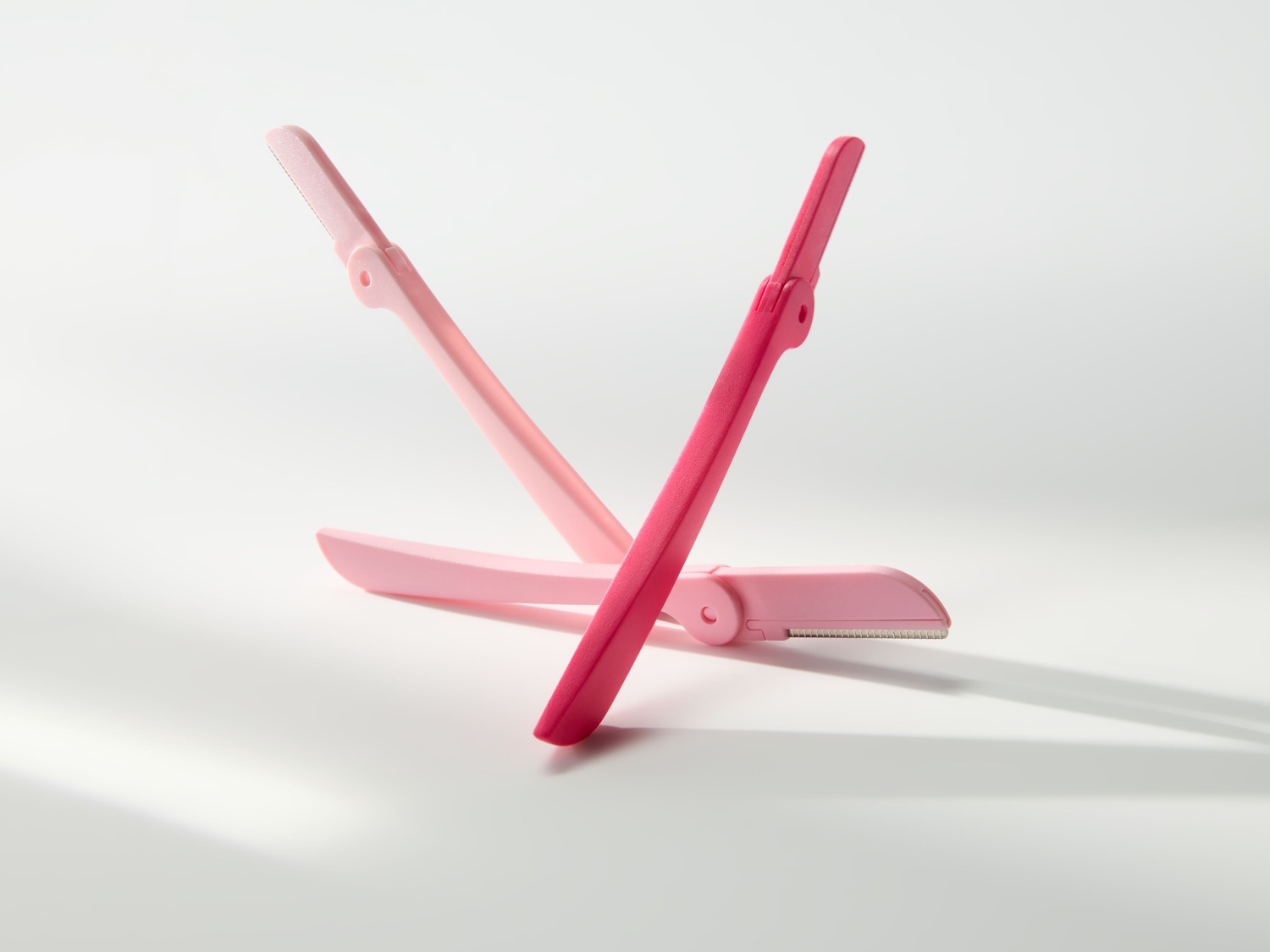 Dos depiladoras faciales de color rosa, una en tono rosa claro y otra en rosa intenso, cruzadas sobre un fondo blanco.