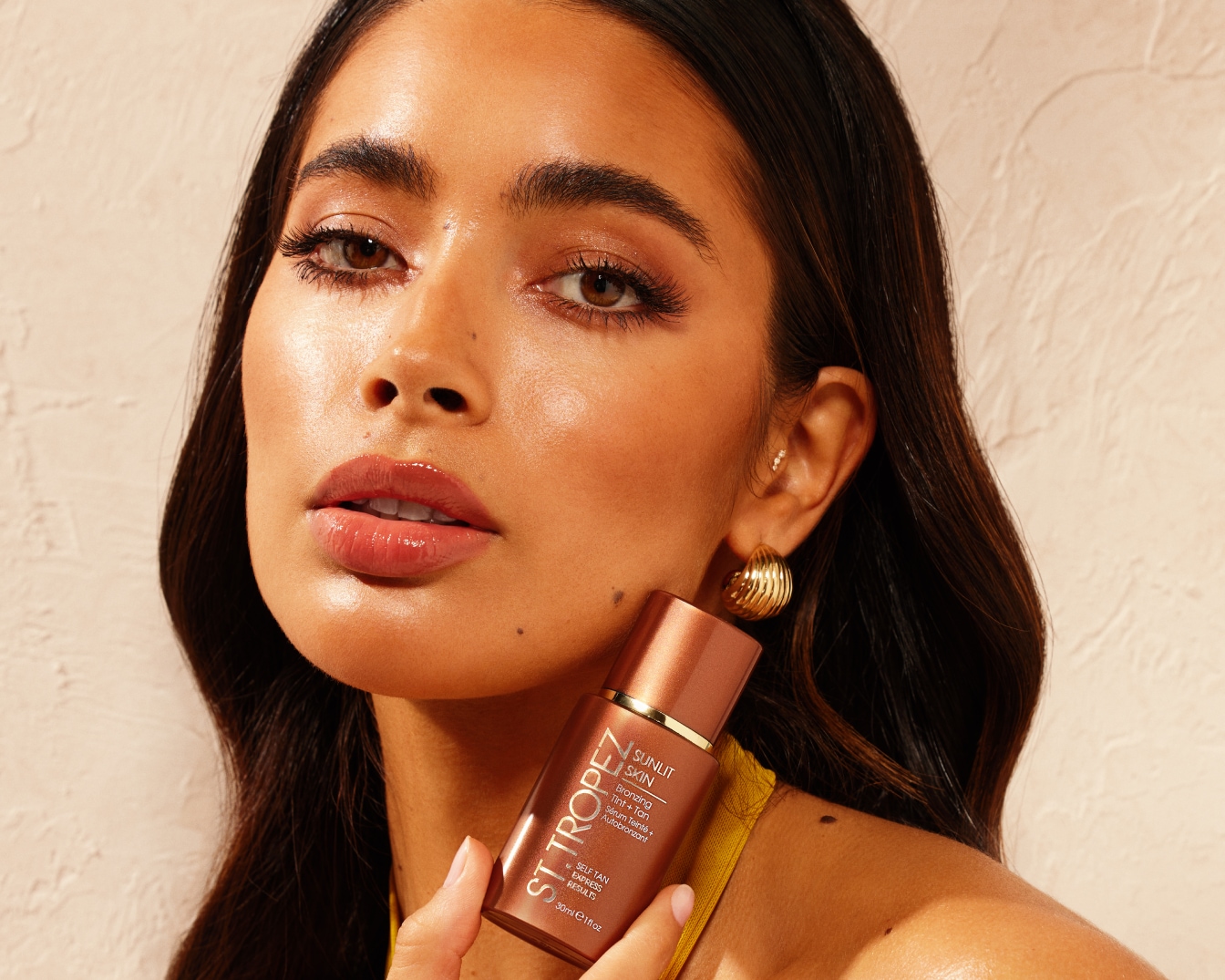 A modell ST. TROPEZ Sunlit Skin bronzosító szérumot tartja, mely önbarnító hatású és azonnali eredményt ígér.